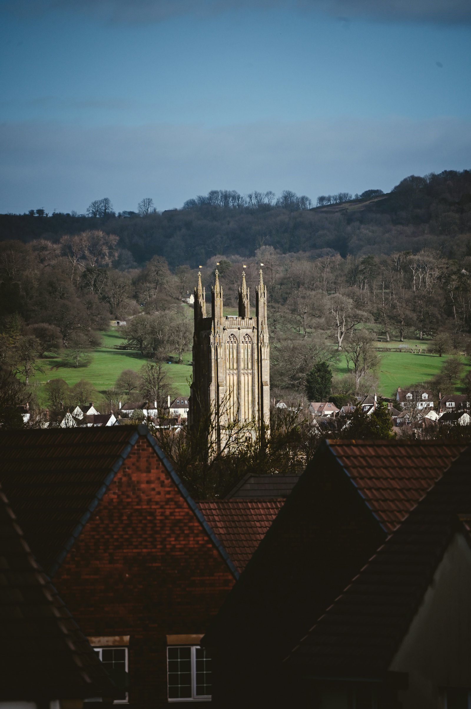 A church tower above village rooftops and surrounding green hills